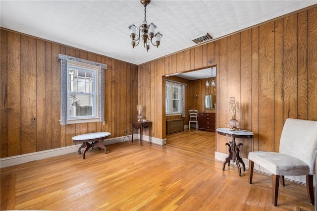 living area with wooden walls, baseboards, visible vents, light wood-type flooring, and a notable chandelier