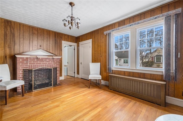 living area featuring light wood-style floors, radiator heating unit, and a brick fireplace