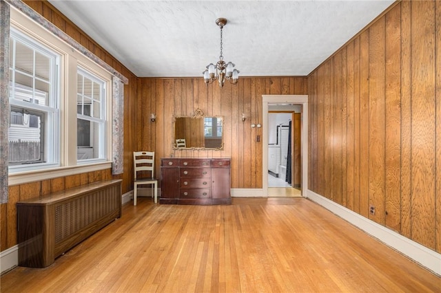 unfurnished dining area featuring radiator, an inviting chandelier, wood finished floors, and wood walls