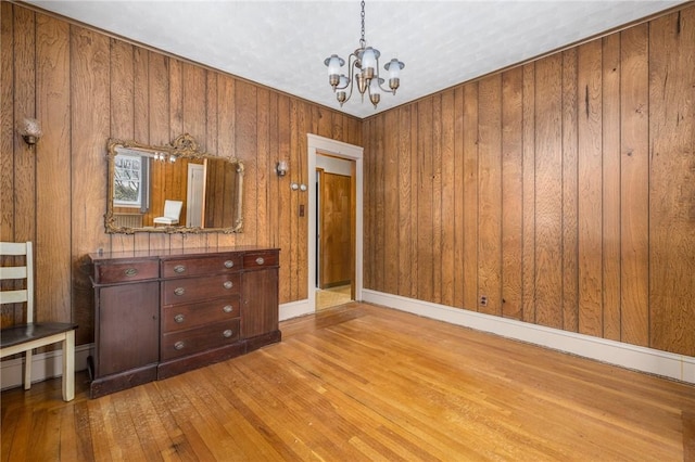 interior space with baseboards, wooden walls, an inviting chandelier, and hardwood / wood-style flooring