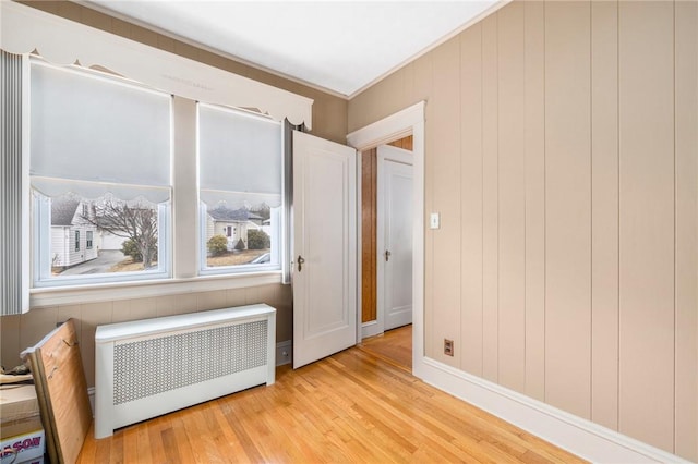 empty room featuring crown molding, light wood-style flooring, and radiator heating unit