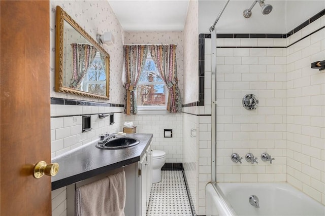 full bathroom with toilet, a wainscoted wall, tile walls,  shower combination, and wallpapered walls