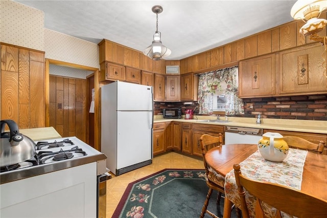 kitchen with white appliances, a sink, light countertops, brown cabinets, and wallpapered walls