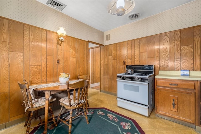 kitchen with brown cabinetry, visible vents, gas range gas stove, and wallpapered walls