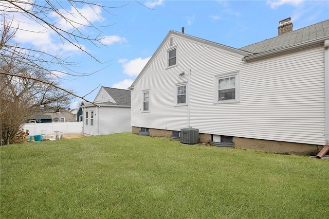 back of house featuring central AC unit, a chimney, fence, and a lawn