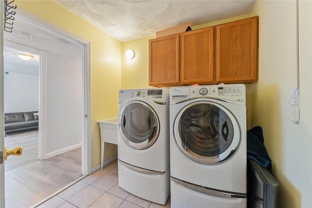 laundry area featuring a textured ceiling, light tile patterned flooring, washing machine and dryer, baseboards, and cabinet space