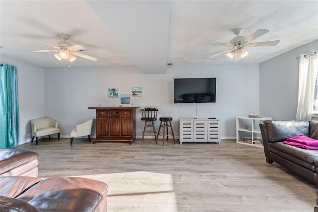 living room featuring ceiling fan, light wood-style flooring, and baseboards