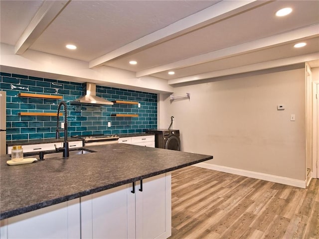 kitchen with light wood-type flooring, wall chimney range hood, tasteful backsplash, and beamed ceiling