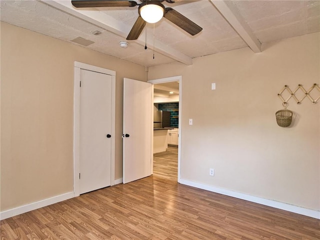 empty room featuring light wood finished floors, a ceiling fan, baseboards, and beam ceiling