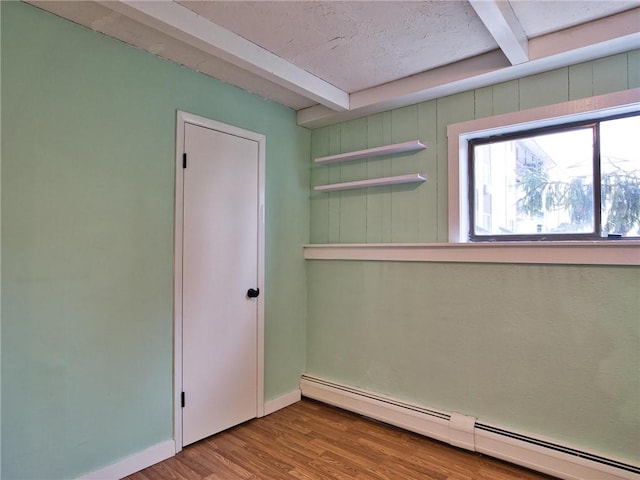 unfurnished room featuring a baseboard radiator, baseboards, beam ceiling, and wood finished floors