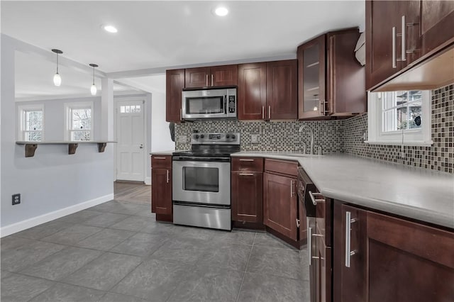 kitchen featuring baseboards, a sink, glass insert cabinets, appliances with stainless steel finishes, and backsplash