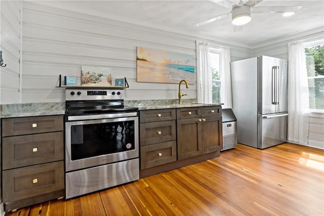 kitchen with light stone counters, stainless steel appliances, a ceiling fan, dark brown cabinets, and light wood-type flooring