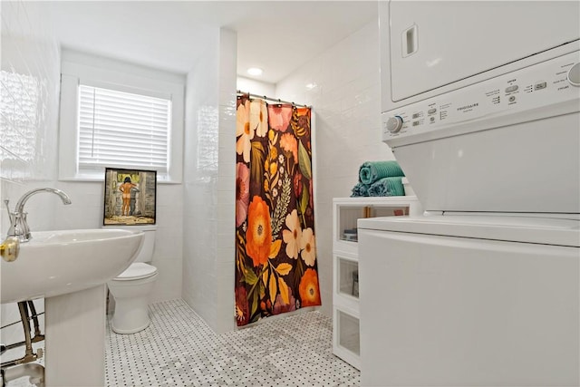 bathroom featuring toilet, tile walls, stacked washer and clothes dryer, and a shower with curtain