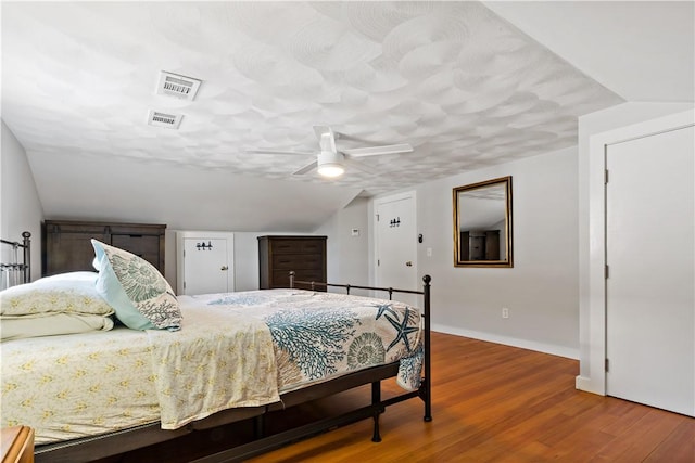 bedroom with ceiling fan, wood finished floors, visible vents, baseboards, and vaulted ceiling