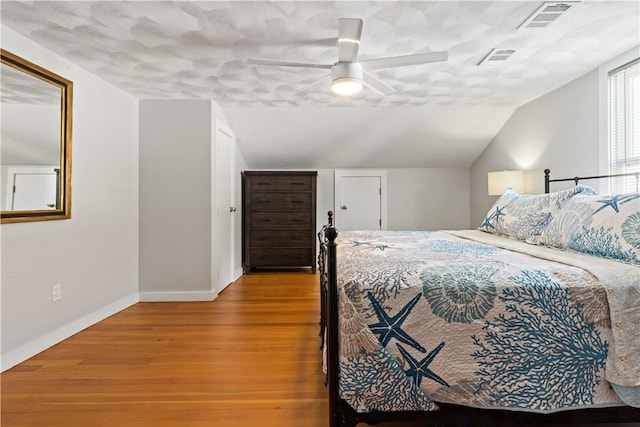 bedroom with lofted ceiling, wood finished floors, visible vents, and baseboards