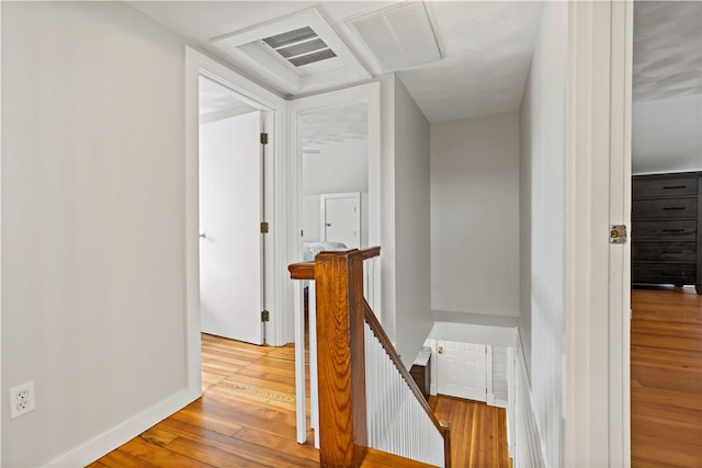 corridor featuring baseboards, visible vents, an upstairs landing, and wood finished floors