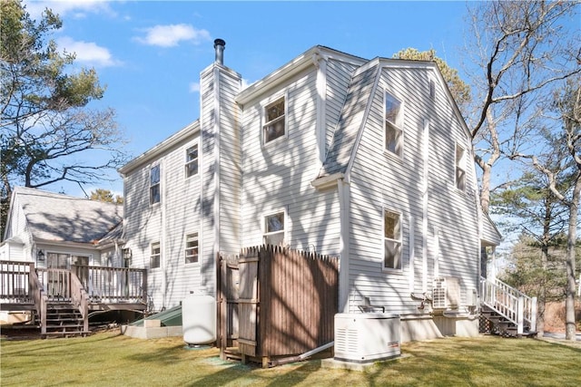 view of side of home with a shingled roof, a lawn, a gambrel roof, a chimney, and a deck