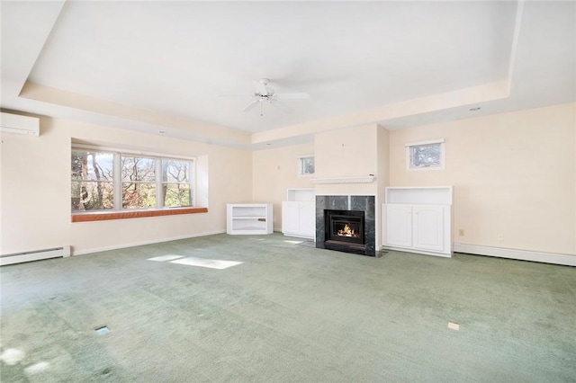 unfurnished living room with ceiling fan, a wall unit AC, a fireplace, a tray ceiling, and carpet