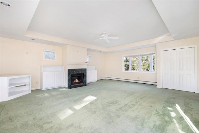 unfurnished living room featuring a high end fireplace, a tray ceiling, carpet flooring, and baseboard heating