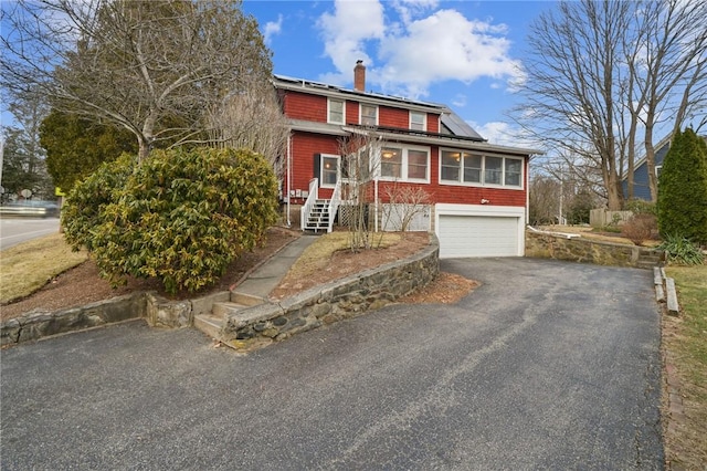 view of front of house with a garage, driveway, roof mounted solar panels, and a chimney