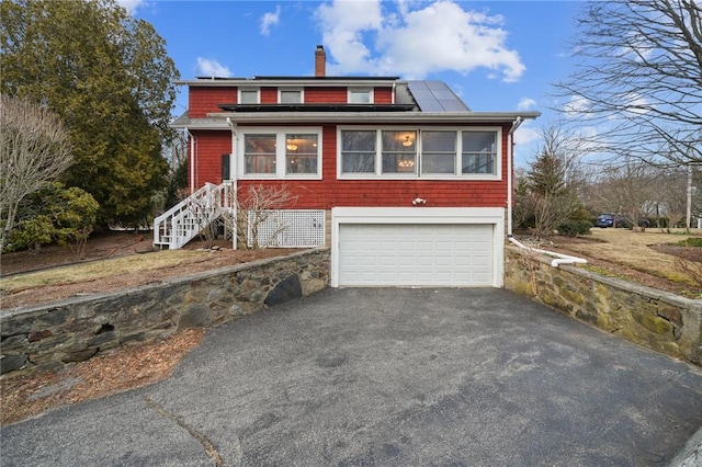 view of front of property featuring aphalt driveway, a chimney, an attached garage, and solar panels