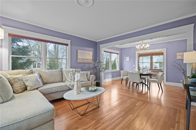 living area with light wood-style floors, crown molding, baseboards, and a notable chandelier