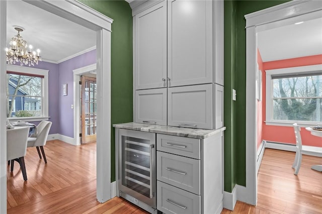 bar featuring a chandelier, light wood-style flooring, beverage cooler, baseboards, and crown molding