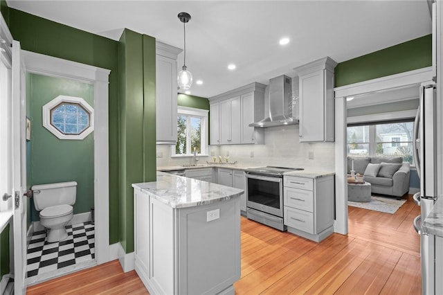 kitchen with stainless steel appliances, a sink, backsplash, light stone countertops, and wall chimney exhaust hood