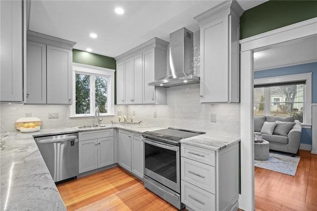 kitchen with wall chimney exhaust hood, appliances with stainless steel finishes, a sink, and light stone countertops