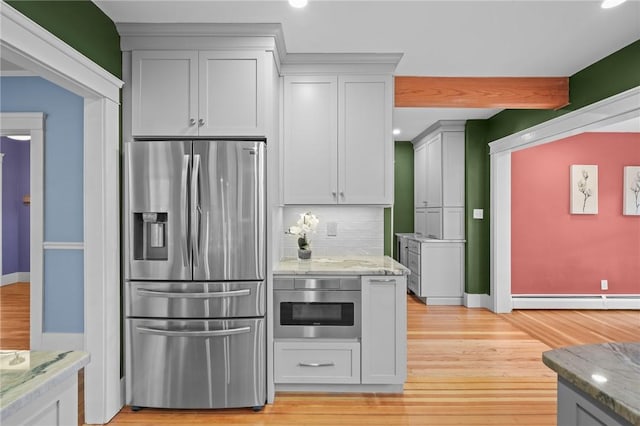 kitchen with stainless steel refrigerator with ice dispenser, light wood finished floors, baseboard heating, decorative backsplash, and light stone countertops