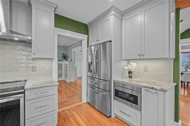 kitchen featuring appliances with stainless steel finishes, light wood-style flooring, wall chimney exhaust hood, and light stone countertops