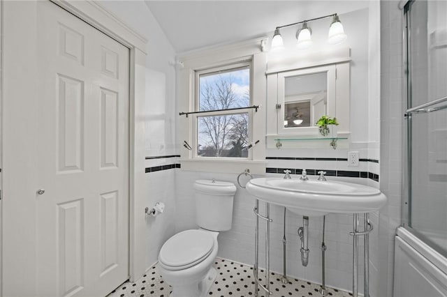 bathroom featuring toilet, a shower with shower door, tile walls, and a wainscoted wall