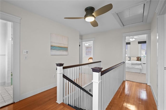 hallway featuring attic access, baseboards, an upstairs landing, and hardwood / wood-style flooring