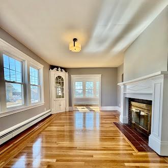 unfurnished living room with a fireplace with flush hearth, plenty of natural light, baseboard heating, and wood finished floors