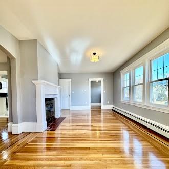 unfurnished living room featuring a fireplace with flush hearth, baseboards, baseboard heating, and wood finished floors