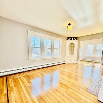 unfurnished living room with a baseboard heating unit, baseboard heating, and wood finished floors