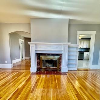 unfurnished living room with a fireplace, baseboards, arched walkways, and wood finished floors