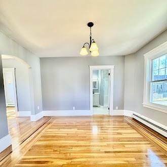 spare room featuring a baseboard radiator, baseboards, a chandelier, and wood finished floors