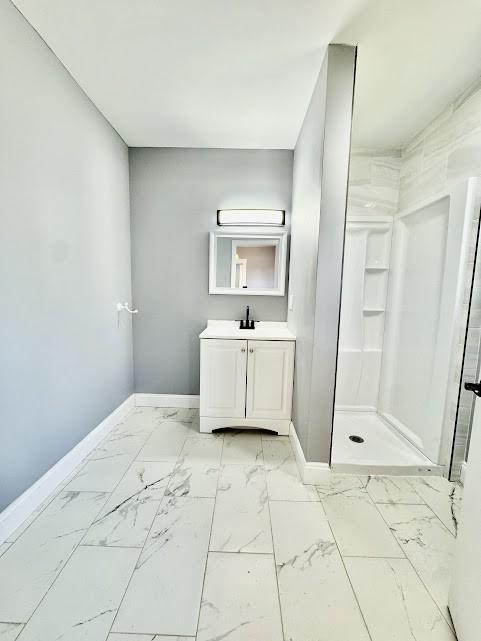 full bathroom with marble finish floor, vanity, baseboards, and a stall shower