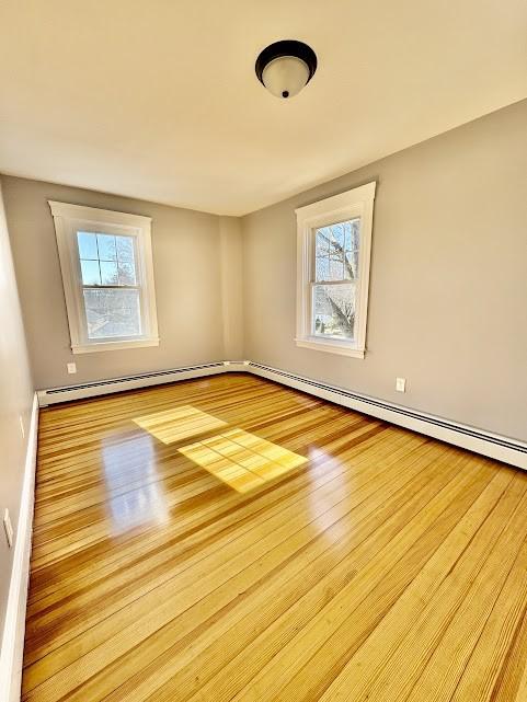 unfurnished room with a baseboard heating unit and wood finished floors