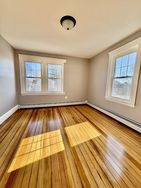 unfurnished room featuring hardwood / wood-style flooring, a baseboard radiator, and baseboards