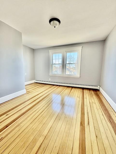 empty room with wood-type flooring, a baseboard radiator, and baseboards