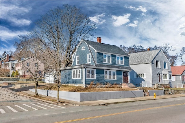 view of front of home featuring a chimney, a residential view, a gambrel roof, and a shingled roof