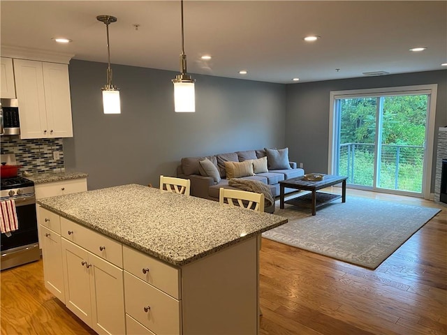 kitchen featuring light wood-type flooring, appliances with stainless steel finishes, decorative backsplash, and a center island