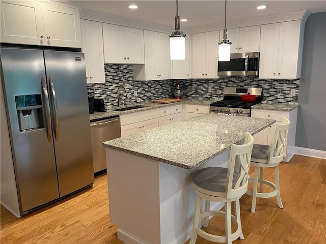 kitchen with light wood finished floors, white cabinets, a kitchen island, stainless steel appliances, and a sink