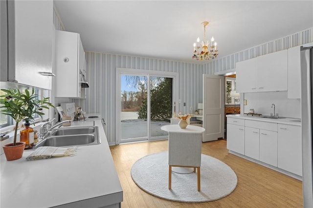 kitchen featuring light countertops, white cabinets, a sink, light wood-type flooring, and wallpapered walls