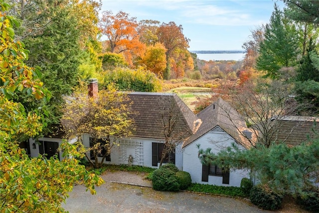 view of front of home with a water view, a shingled roof, a chimney, and brick siding