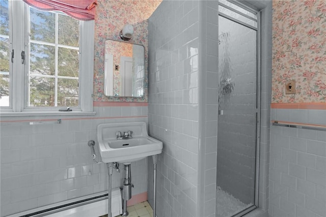 bathroom with a sink, tile walls, wainscoting, a stall shower, and wallpapered walls