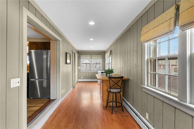 hallway with light wood finished floors, baseboard heating, a baseboard radiator, and recessed lighting