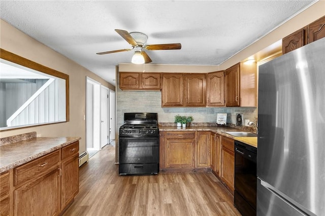 kitchen with a sink, light wood finished floors, brown cabinets, black appliances, and tasteful backsplash